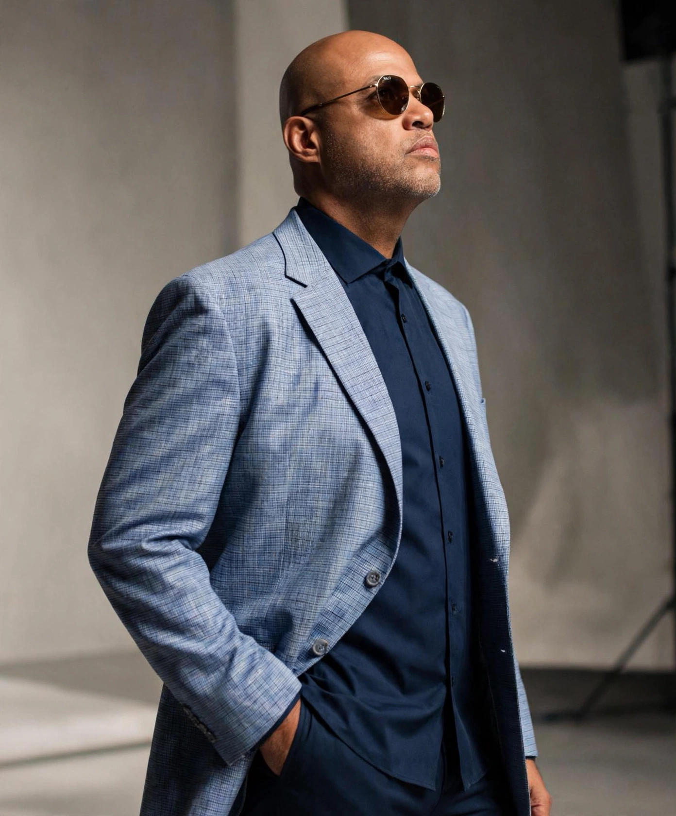 Byron Jupiter in a light blue linen blazer and navy shirt, photographed against a grey studio backdrop.