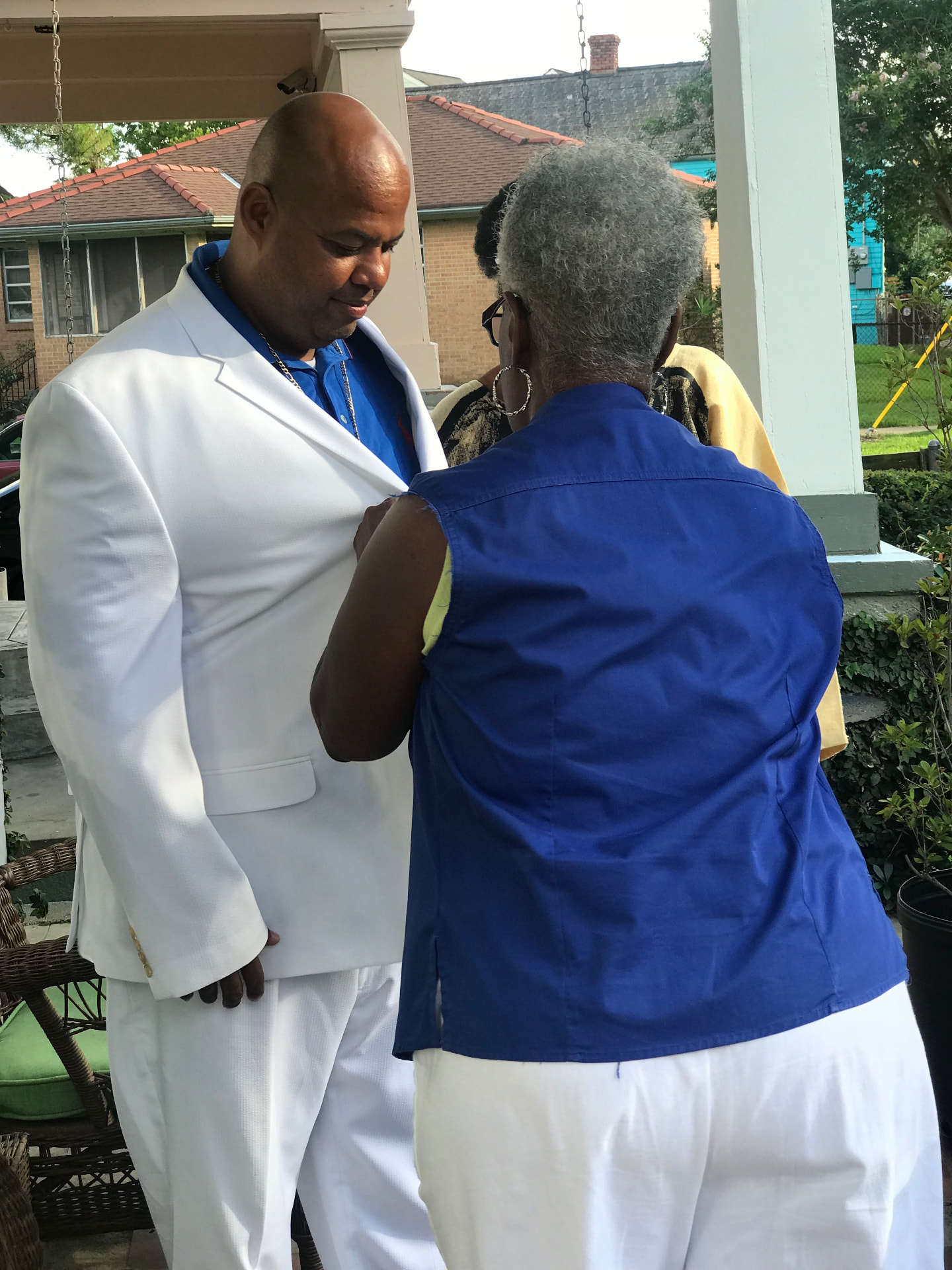 Momma Peggy fixing the lapel of her son's white suit jacket on a porch before an event.