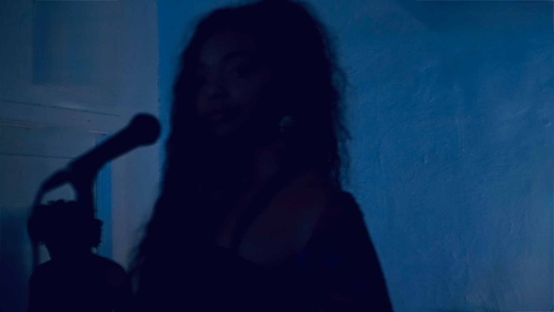 Aaniyah at the microphone under blue light, silhouette against the wall
