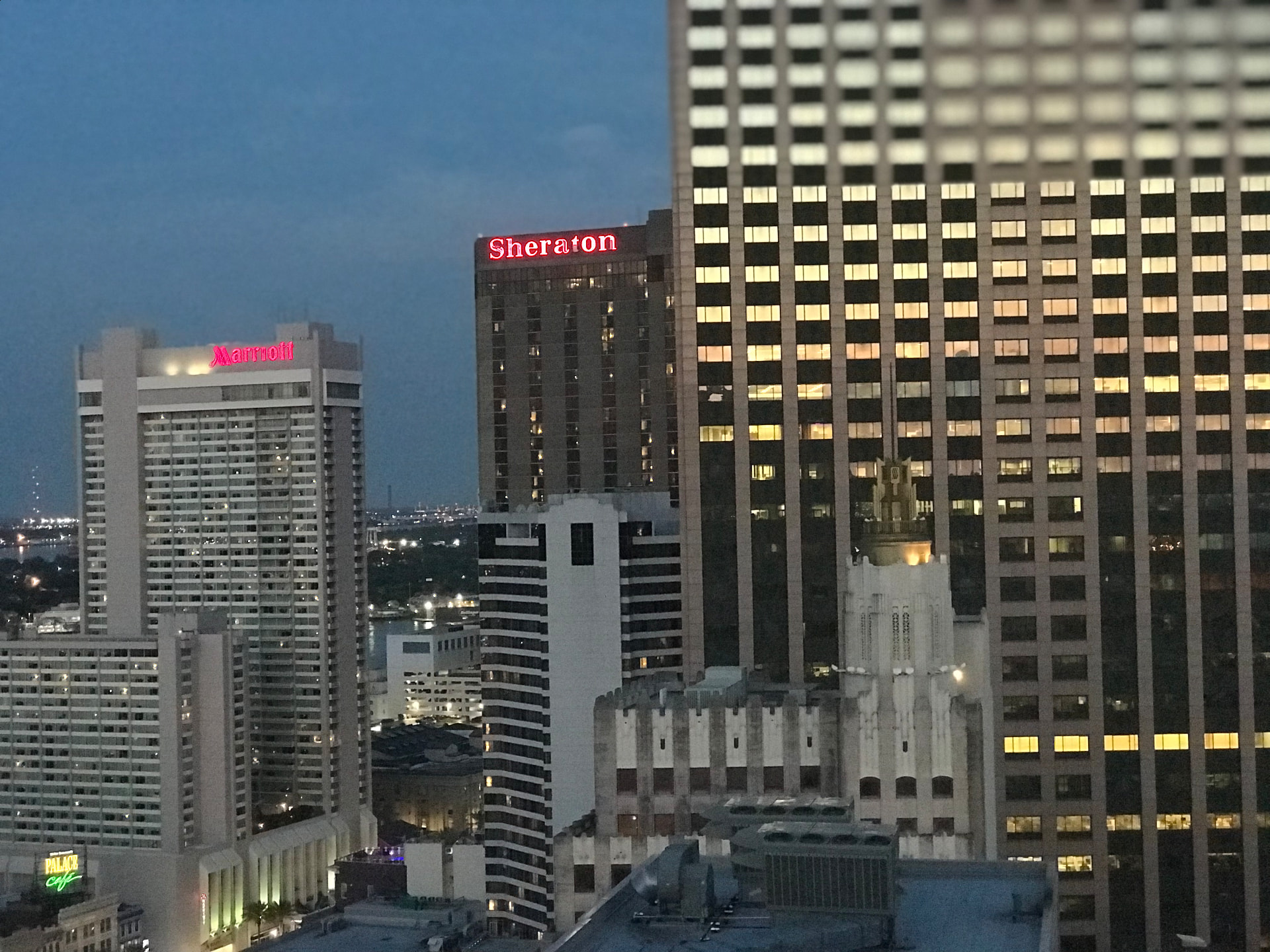 New Orleans Central Business District towers at dusk with lit Sheraton and Marriott signs and the green Palace Café neon below