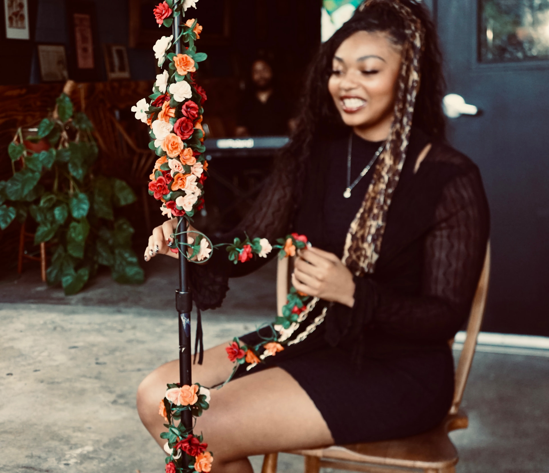 Aaniyah Anderson laughing while winding a floral garland around the microphone stand between takes