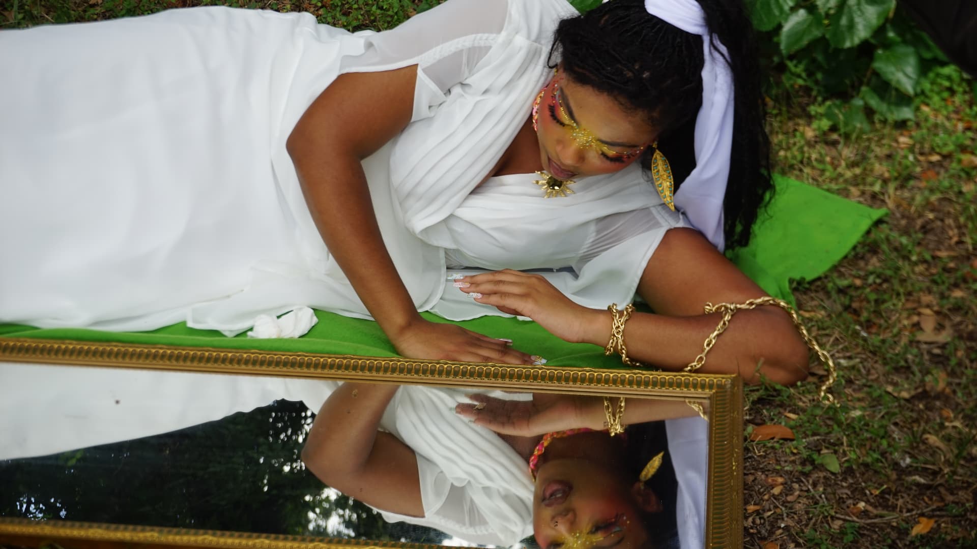 Overhead frame of Aaniyah reclining beside a gold-framed mirror, her reflection visible