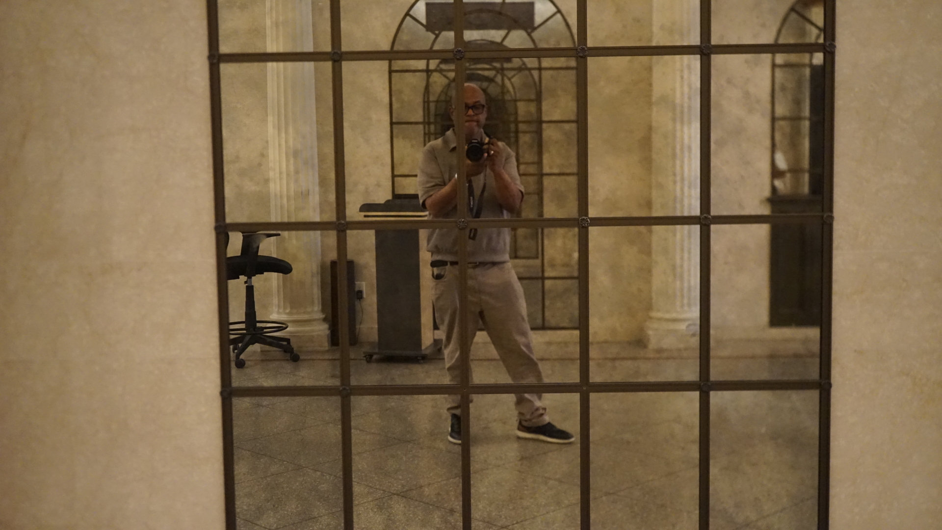 Archive photographer reflected in a leaded-glass window inside a marble hall.