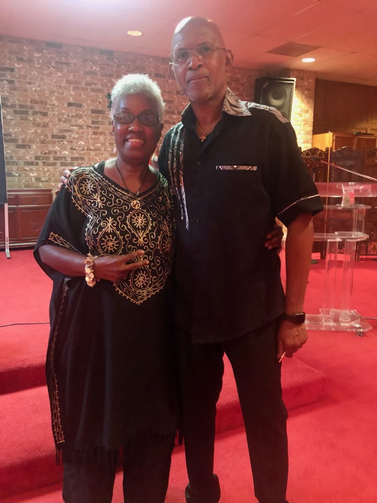 Momma Peggy in a black and gold embroidered dress standing with family inside a church sanctuary.