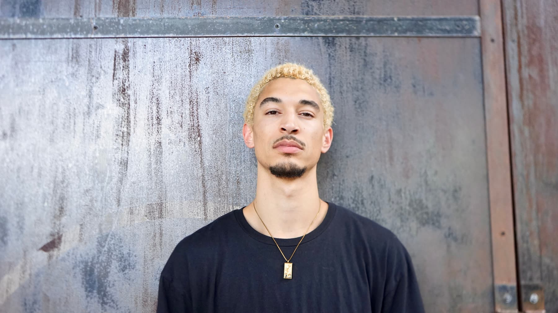 Close portrait of DUS10 showing forearm tattoos and a gold pendant chain