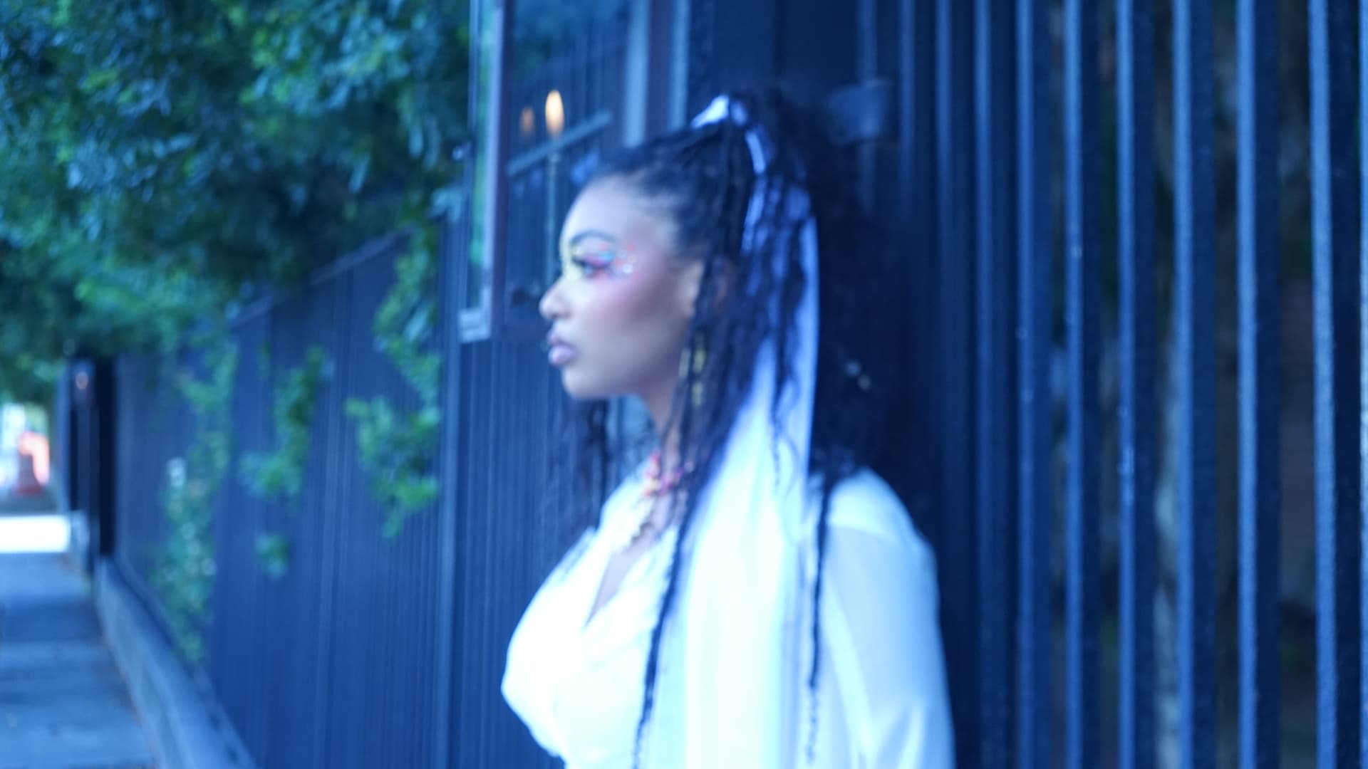 Blue-hour profile of Aaniyah in white against a dark iron fence on the sidewalk