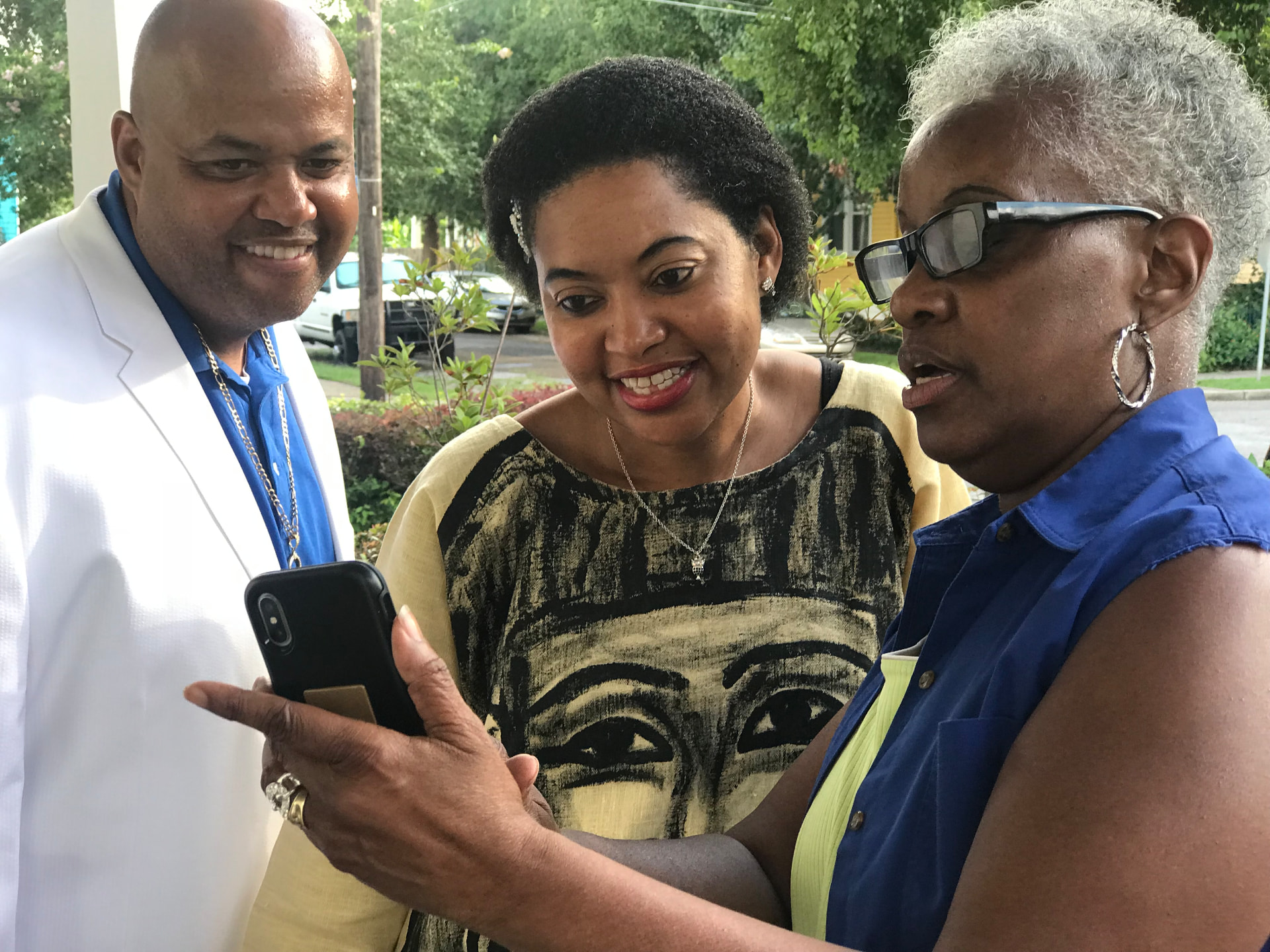 Momma Peggy showing a photo on her phone to family members on a New Orleans porch.